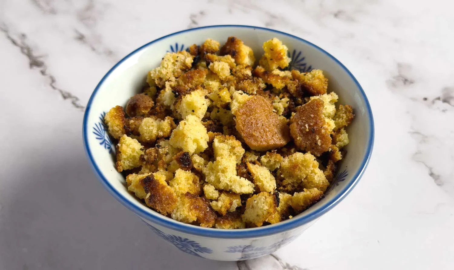 Golden brown bread croutons in a blue-patterned bowl on a marble countertop.